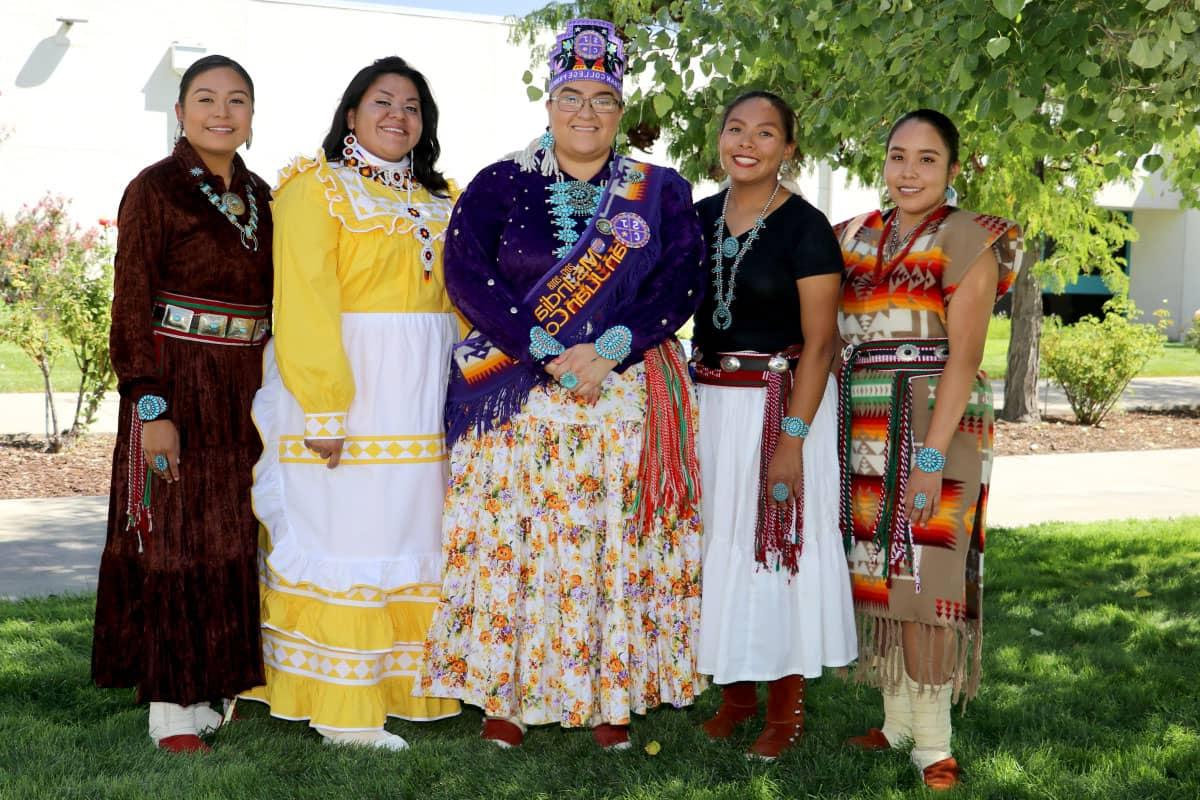 Five individuals pose and smile while wearing native-style dress